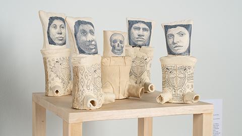 Five ceramic vessels with faces of migrants on them by artist Hugo Crosthwaite.